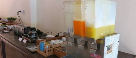 A breakfast bar with a juice dispenser, coffee maker, and various food items.