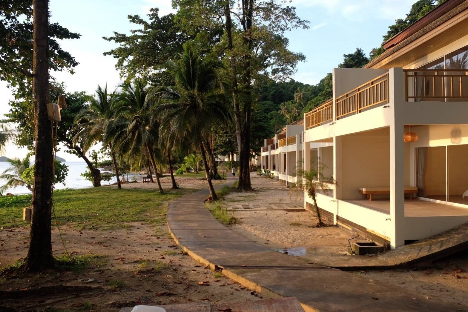 A beachfront resort with modern architecture, a pathway leading to the beach, and palm trees.