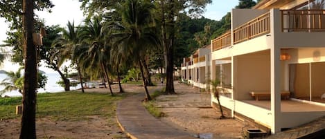 A beachfront resort with modern architecture, a pathway leading to the beach, and palm trees.