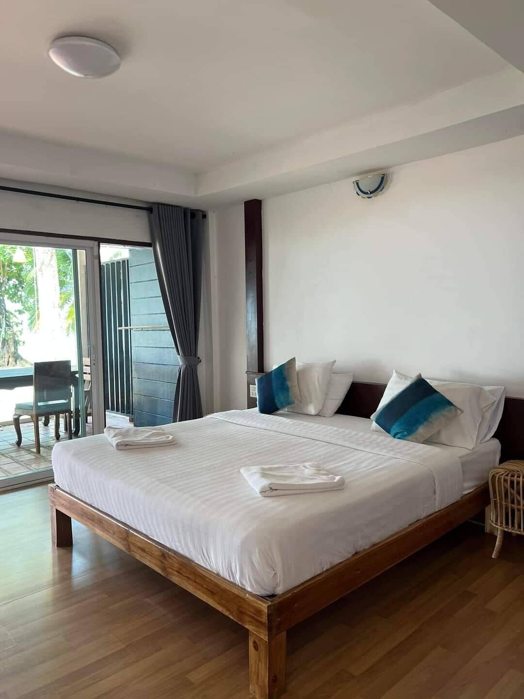 A neatly made bed with white linens and blue pillows, a wooden headboard, and a large window with curtains.