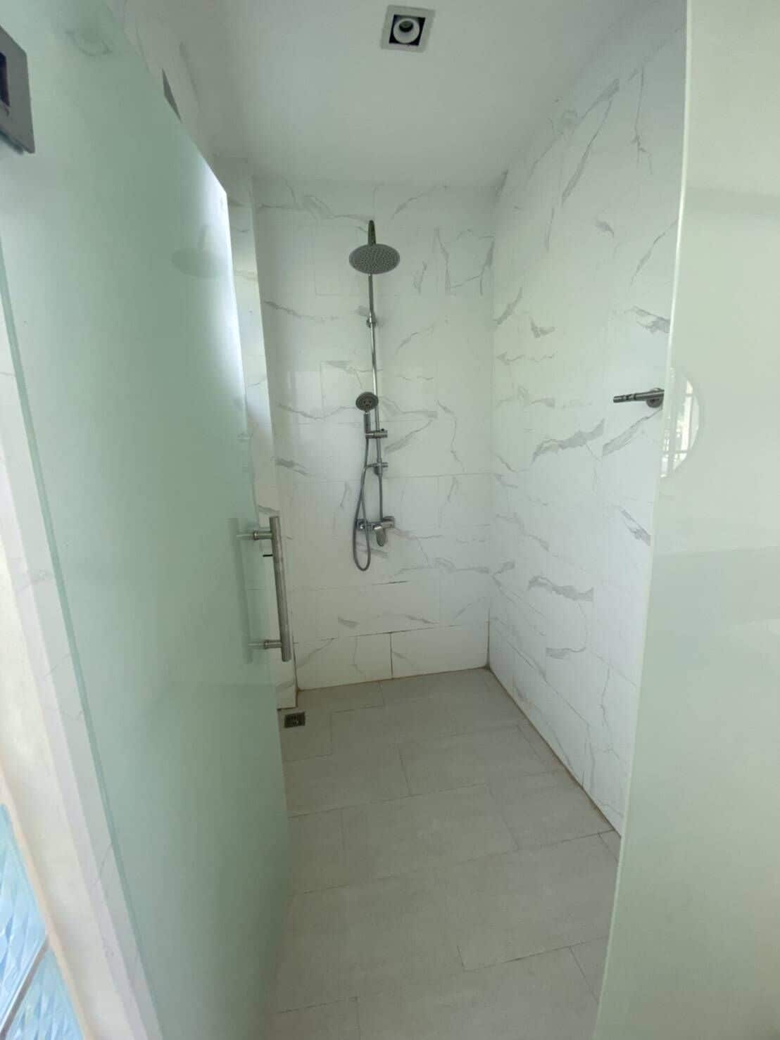 A narrow shower room with white marble walls and floor tiles.