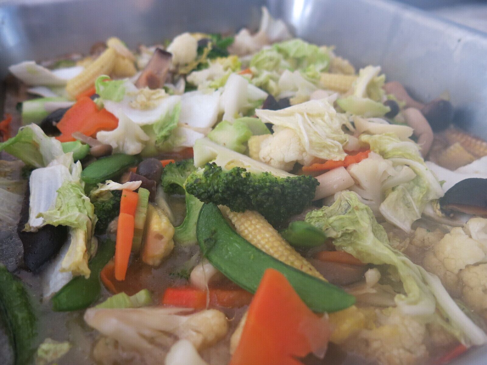 Een roestvrijstalen kookpot gevuld met diverse groenten, waaronder broccoli, wortels en bloemkool.