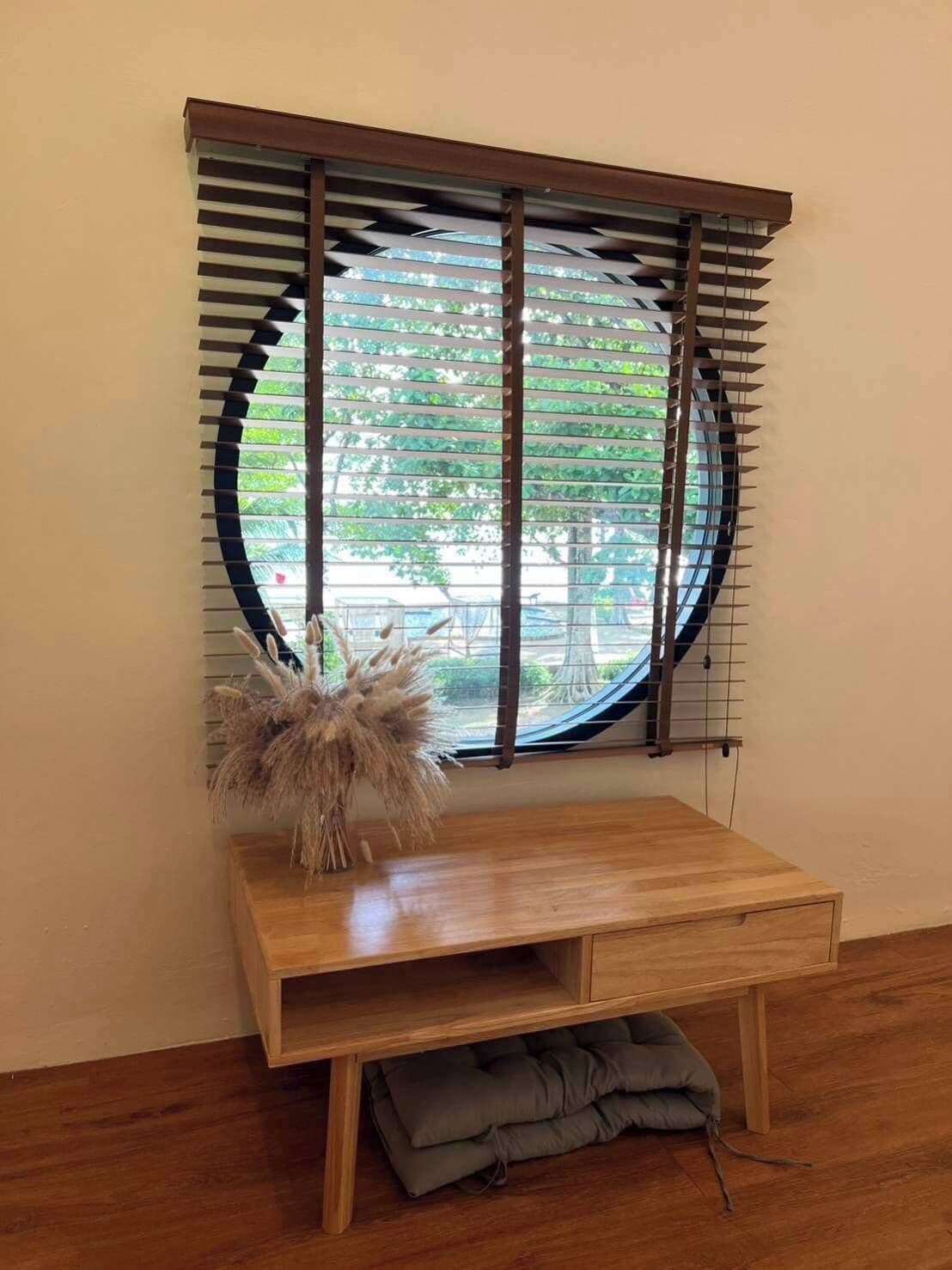A room with a wooden desk, a round window with blinds, and a small plant on the desk.
