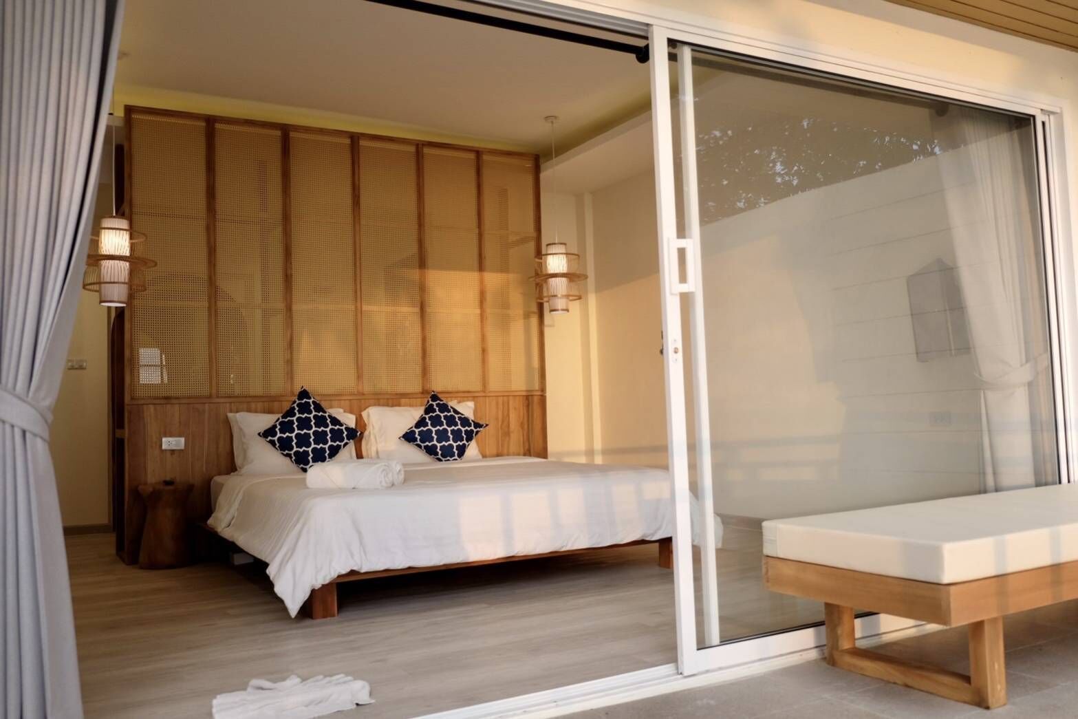 Ein Schlafzimmer mit einem Bett, zwei Kissen, einem Nachttisch und einer Schiebetür zu einem Balkon.