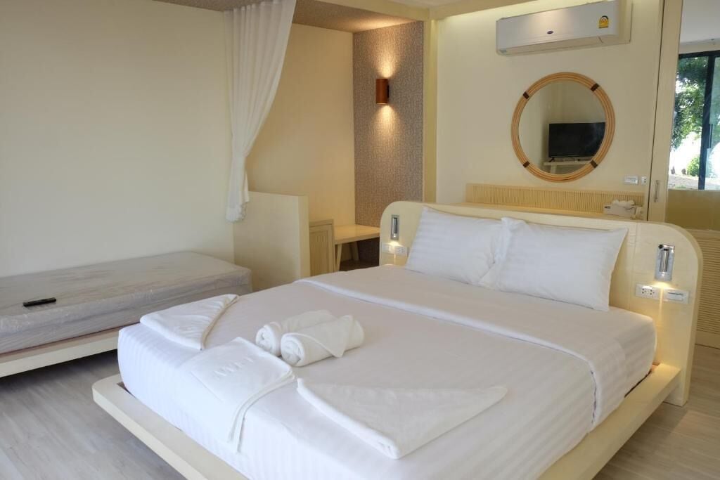 A hotel room with a large bed, a smaller bed, a wall-mounted TV, and a bedside table with a lamp.