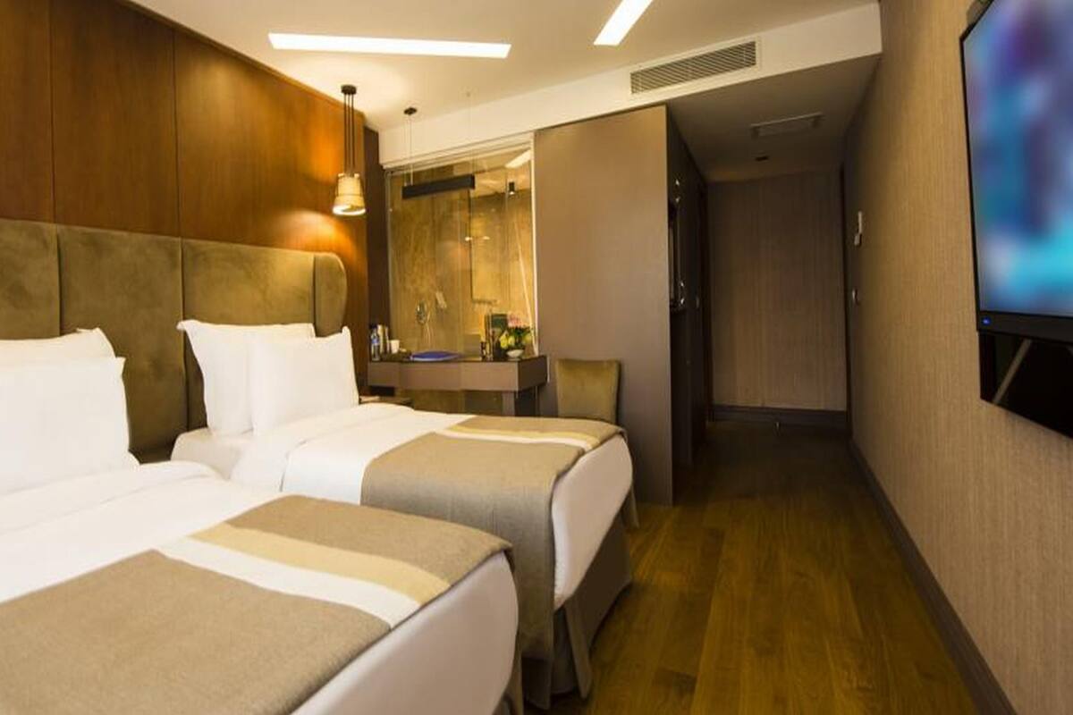A hotel room with two beds, a desk, a mirror, and a television.