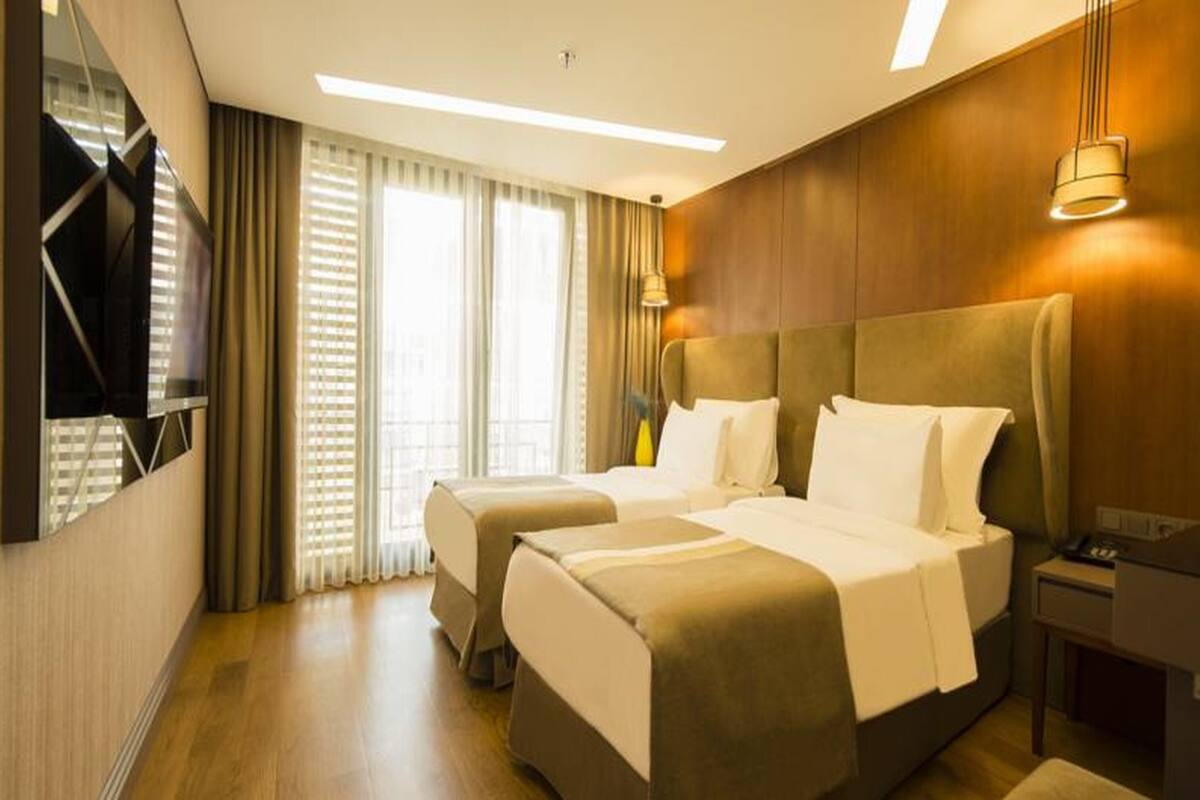 A hotel room with two beds, a TV, a desk, and a window with curtains.