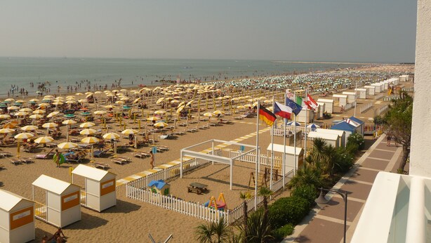 A beach with numerous umbrellas and sun loungers, a fenced play area, and lifeguard towers.