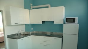 A compact kitchen with white cabinets, a sink, a microwave, and a refrigerator.