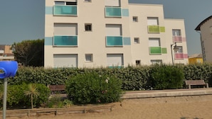 A multi-story building with balconies, a clear sky, and a bench in the foreground.