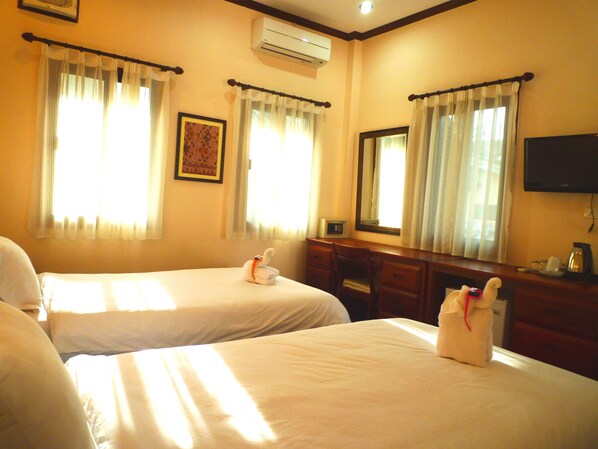 A hotel room with two beds, a desk, a chair, a television, and a window with curtains.