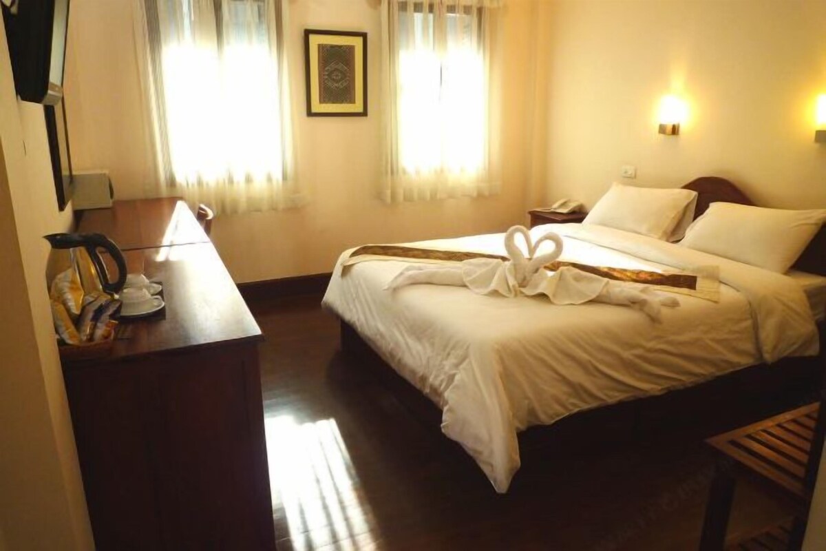 A hotel room with a bed, bedside table, lamp, and curtains.