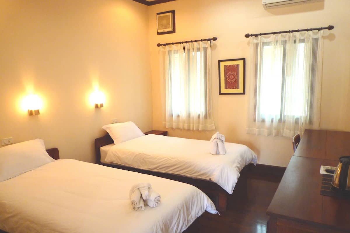 A hotel room with two beds, a wooden desk, and a wall-mounted air conditioner.