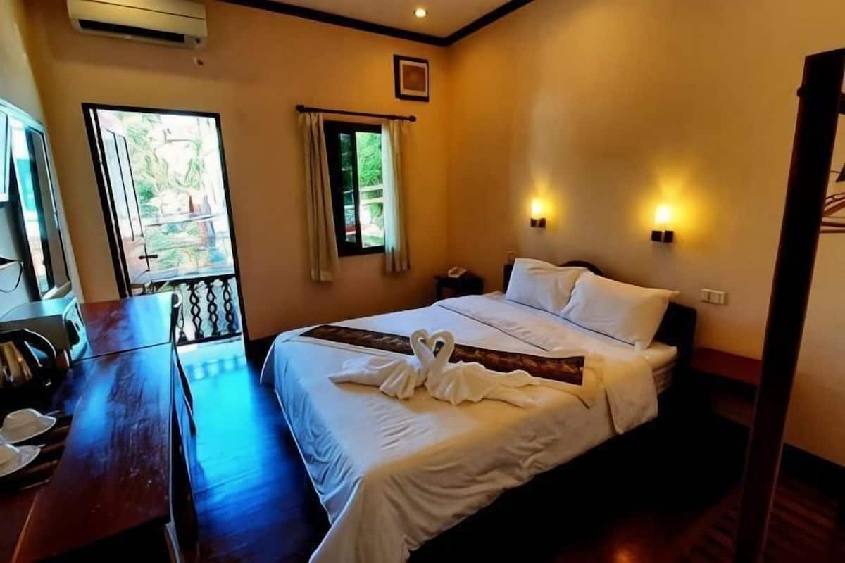 A hotel room with a bed, a desk with a chair, a telephone, and a window with curtains.
