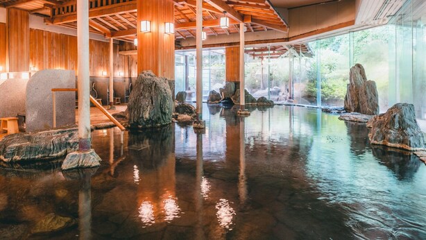 A traditional Japanese onsen with wooden beams, stone baths, and a view of the surrounding forest.