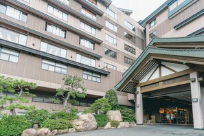 A multi-story hotel with a covered entrance and a landscaped garden area with rocks and trees. - Hotel Gyokusen (Matsue)