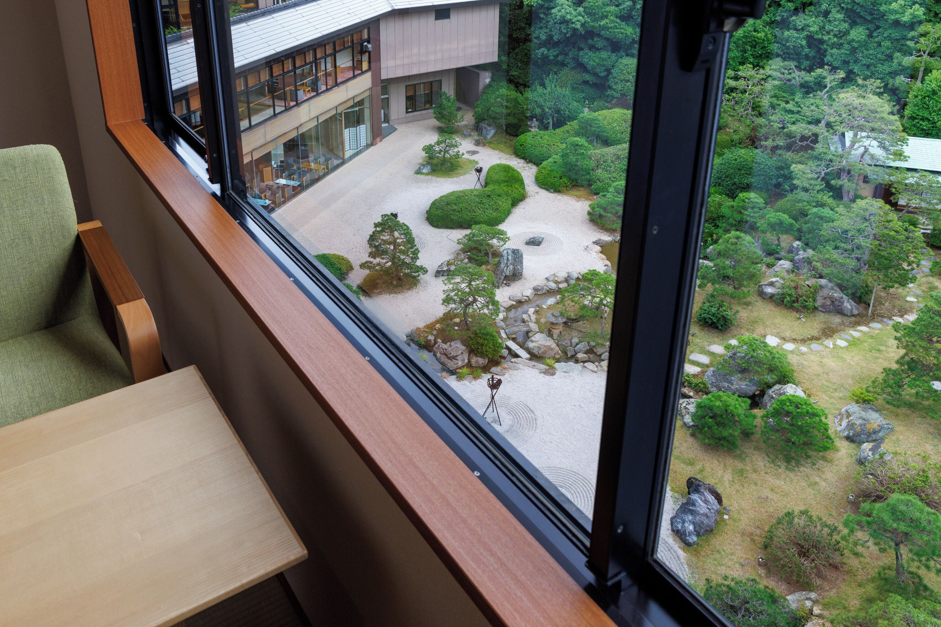 A view from a window of a building with a landscaped garden, a wooden bench, and a table.