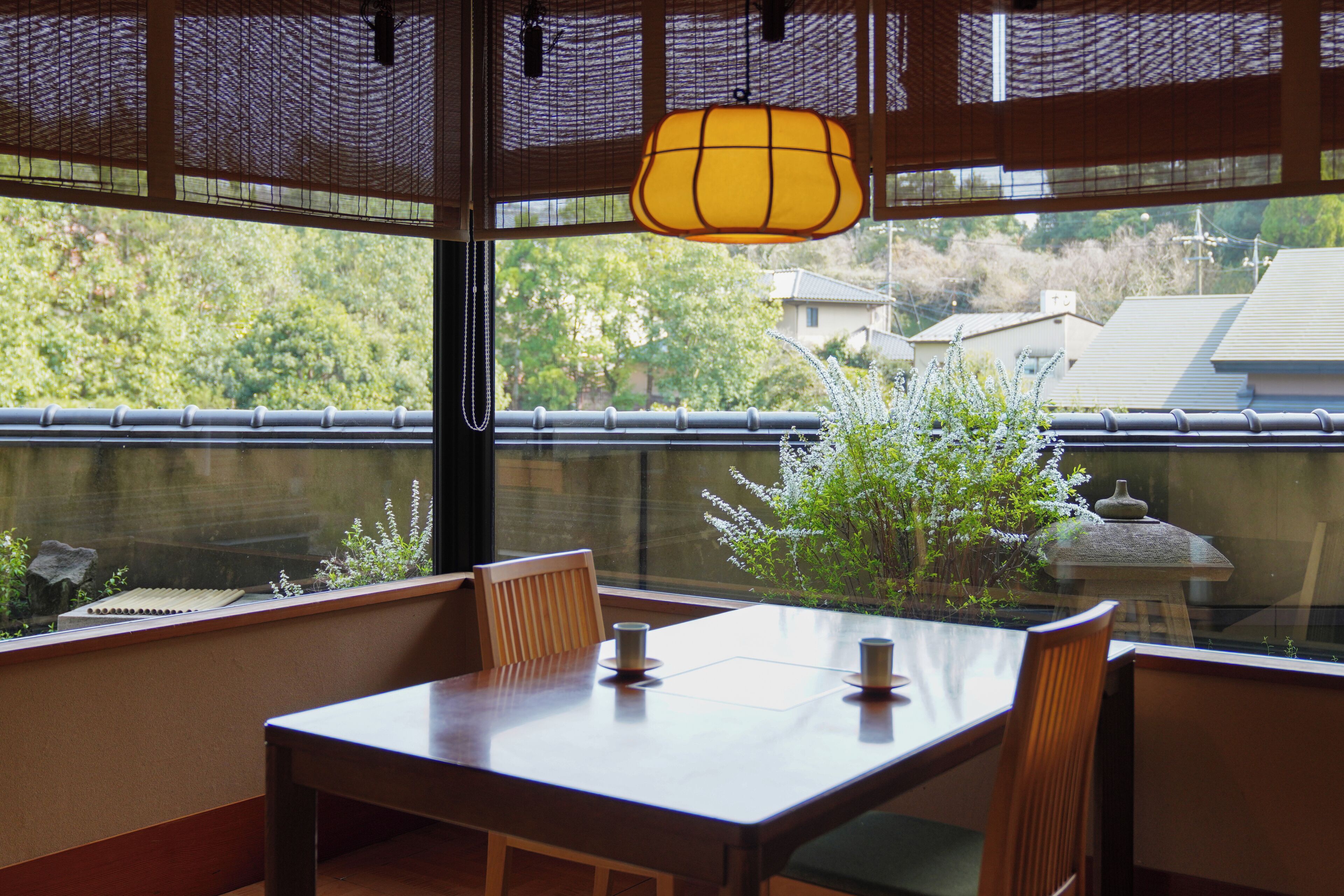 Comedor con mesa y sillas, lámpara colgante, y vistas a zonas verdes y edificios.