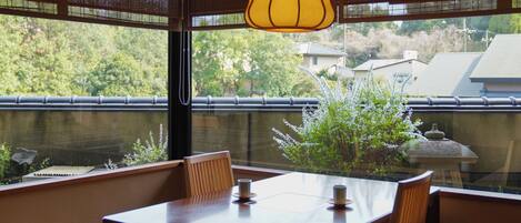 Comedor con mesa y sillas, lámpara colgante, y vistas a zonas verdes y edificios.