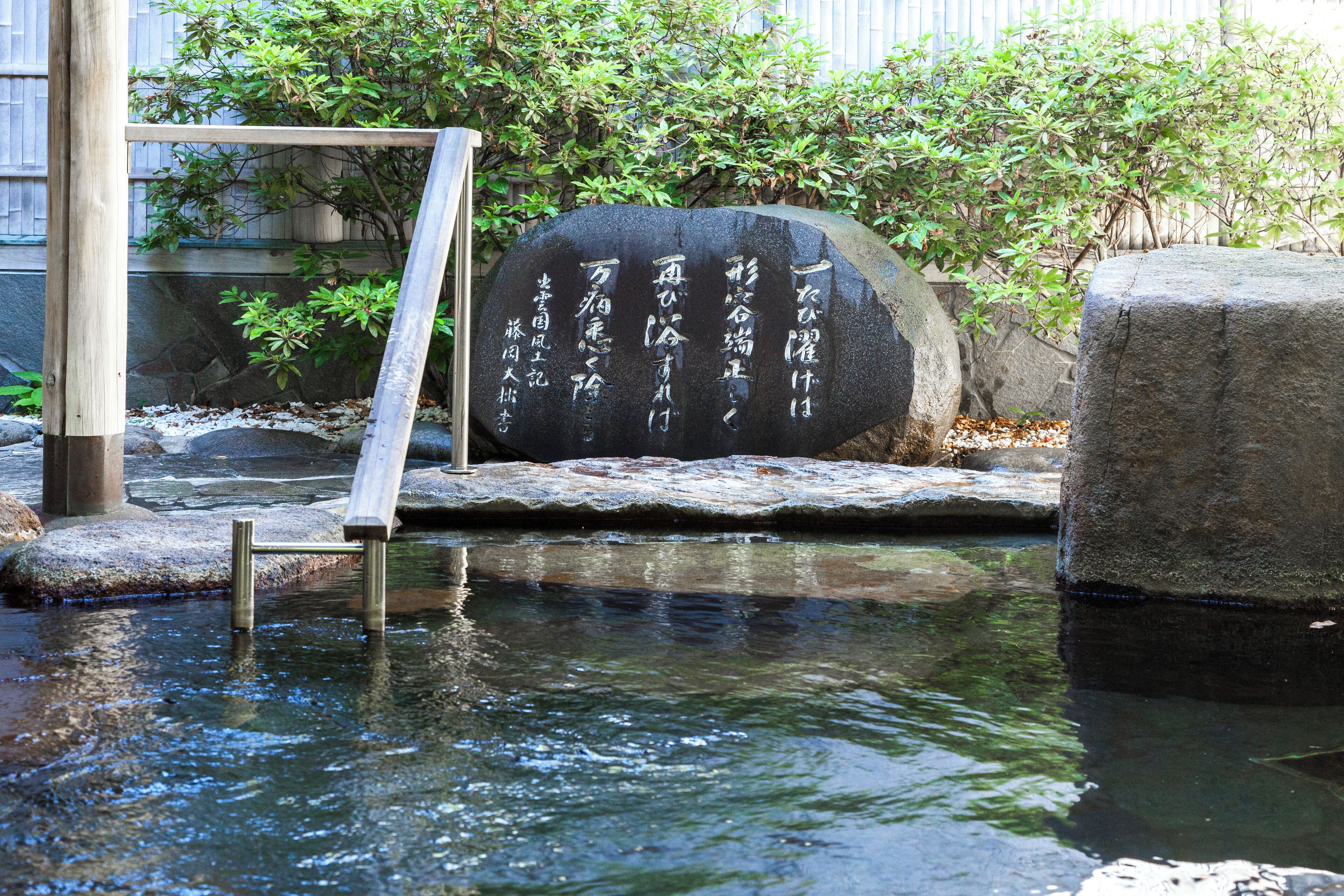 A stone with Japanese characters, a wooden ladder, and a stone platform over water.
