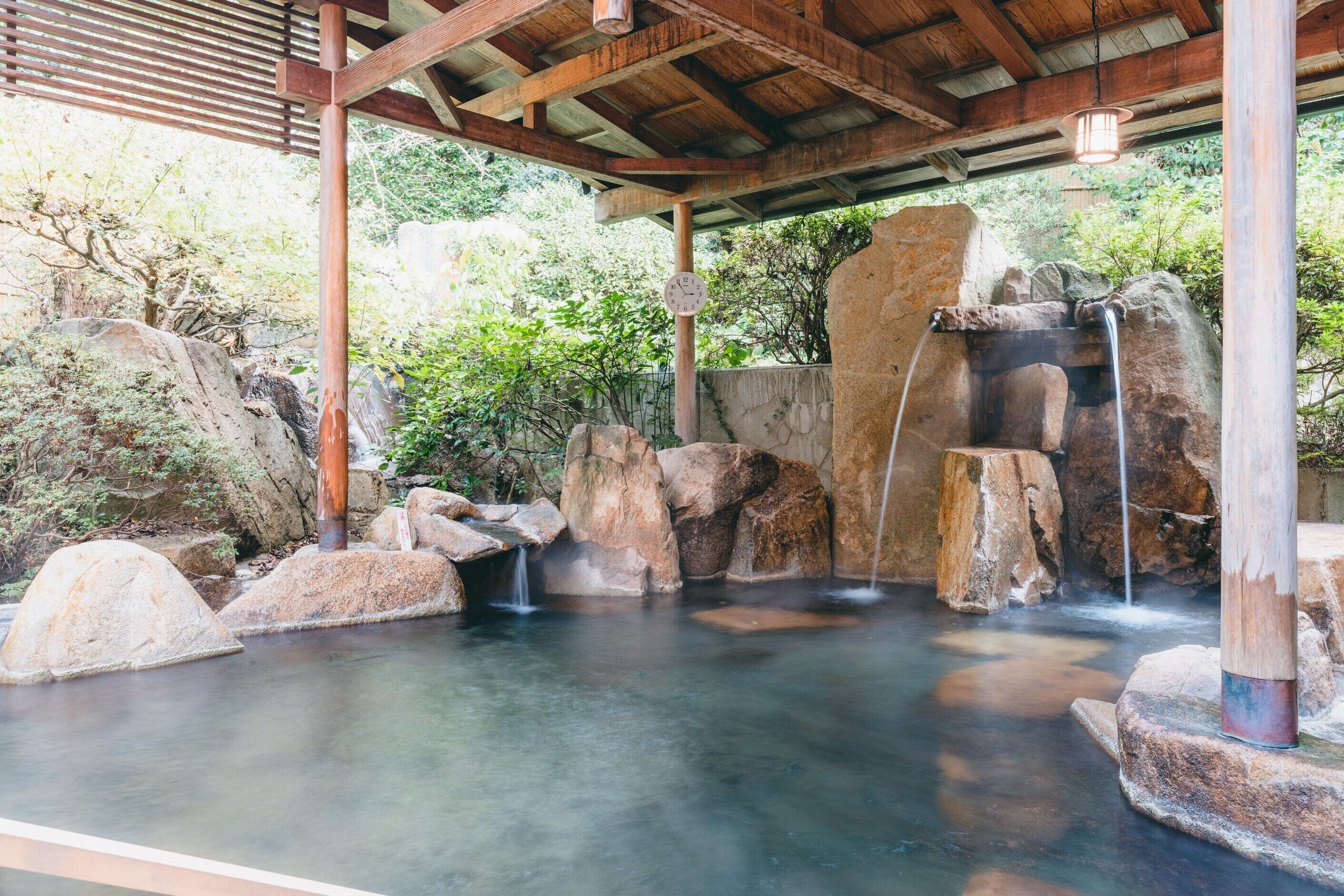 A traditional Japanese onsen with a wooden structure, hot spring pools, and natural rock formations.