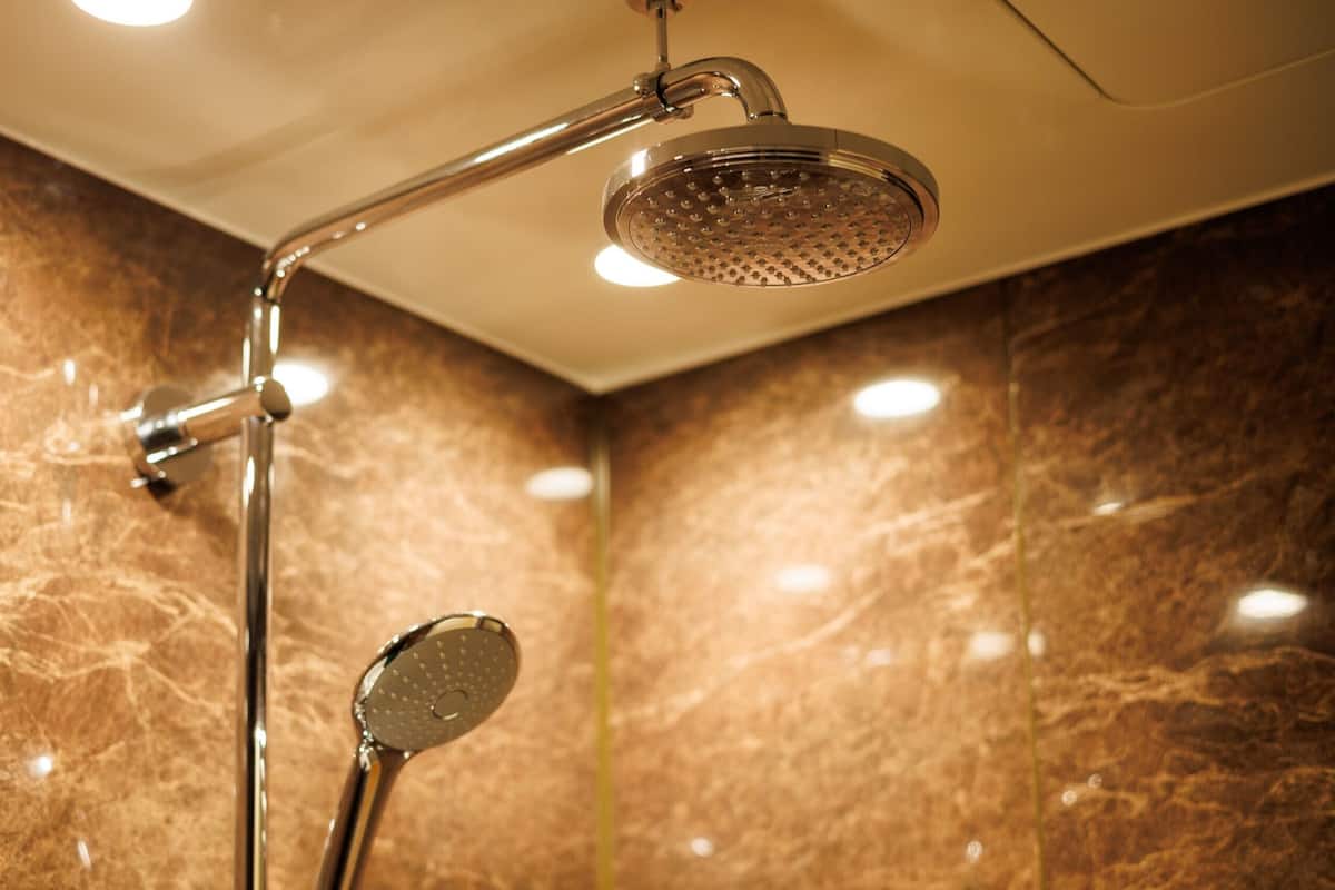 A shower with a handheld showerhead and a fixed overhead showerhead in a bathroom with marble walls.