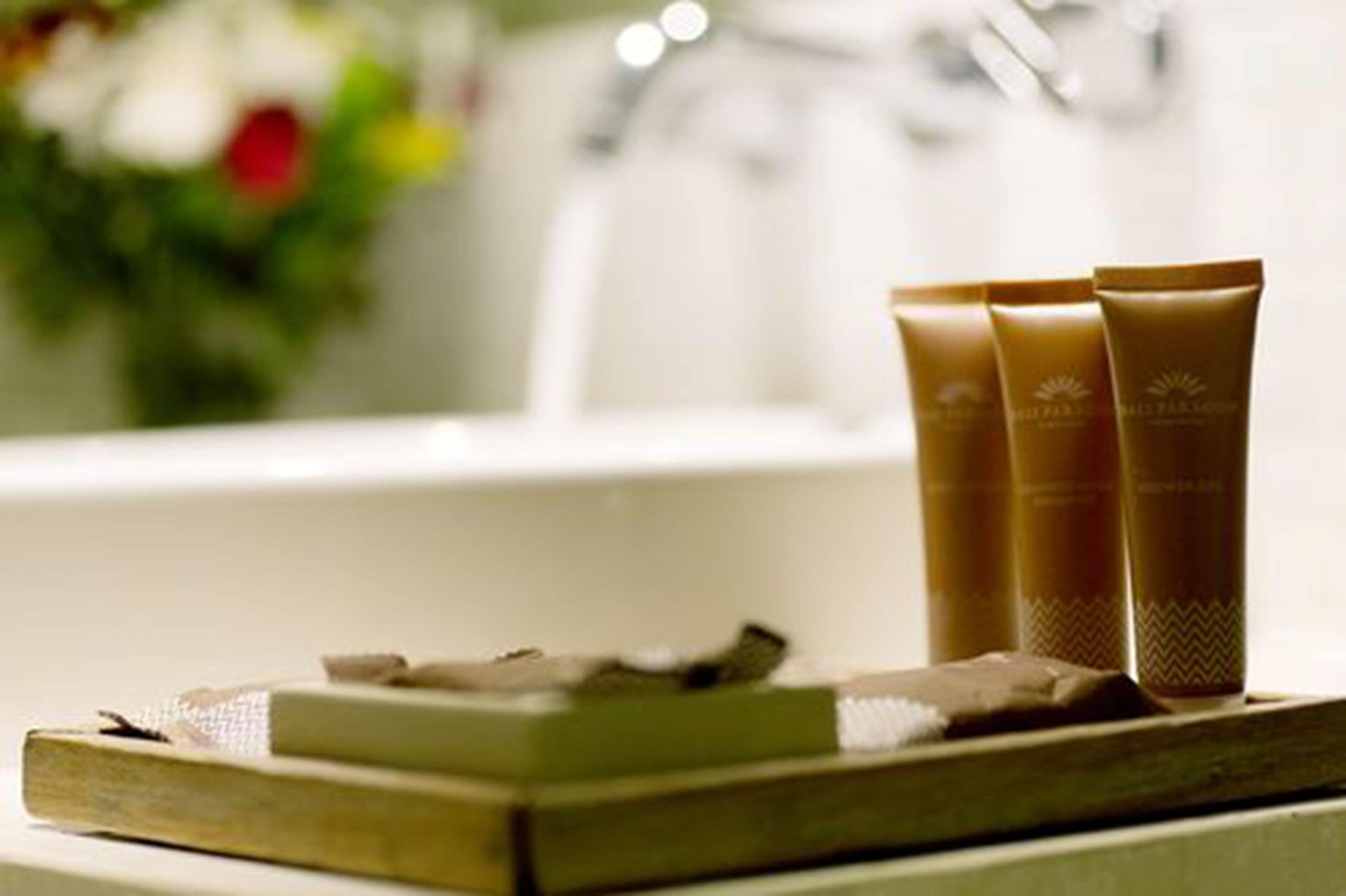 A bathroom with a bathtub, a wooden tray with soap and a towel, and three brown bottles on the edge of the tub.