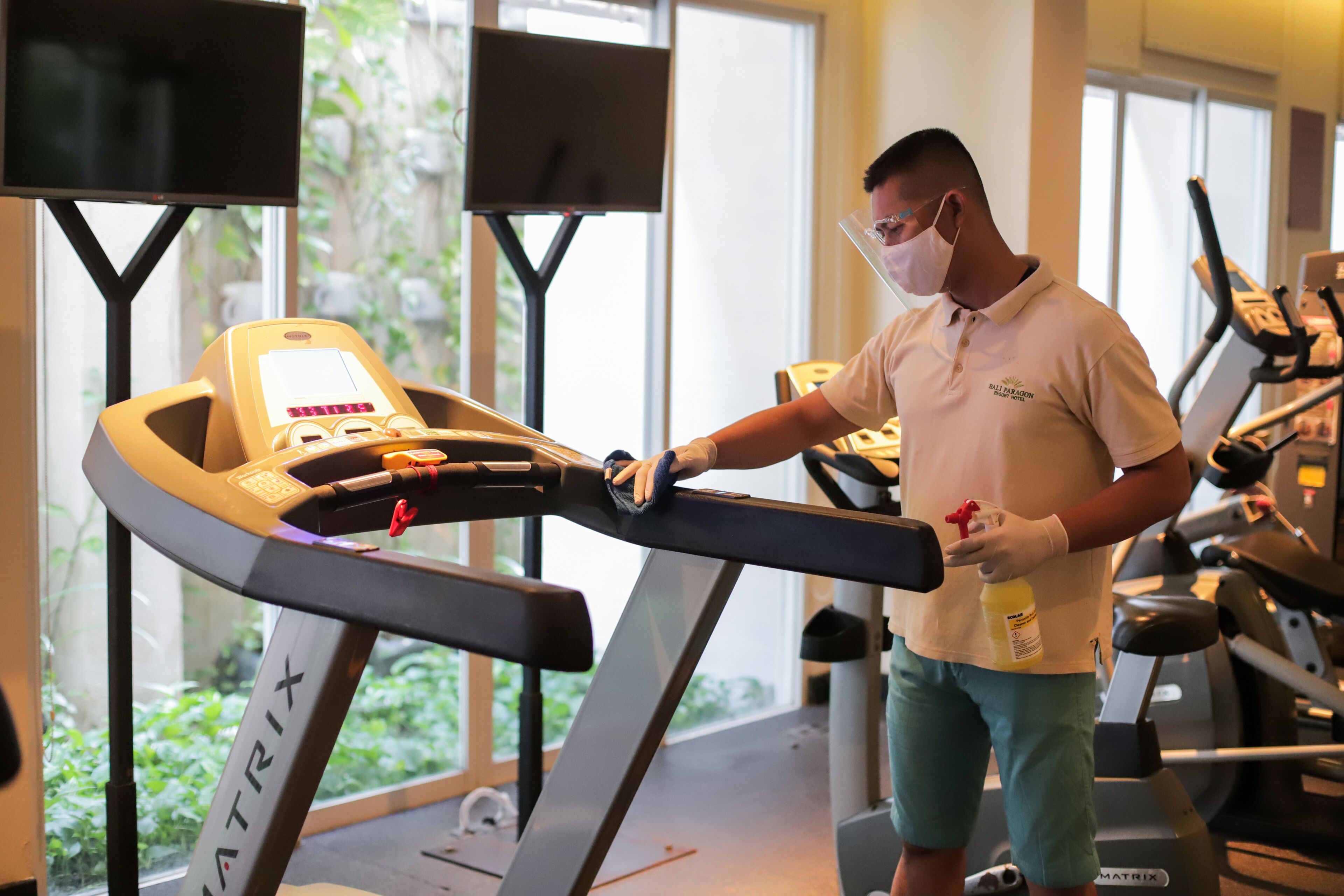 Un uomo utilizza un tapis roulant in palestra, con diversi tapis roulant e una grande vetrata.