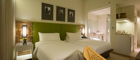 A hotel room with two beds, a green headboard, a nightstand with a lamp, and a wicker chair.