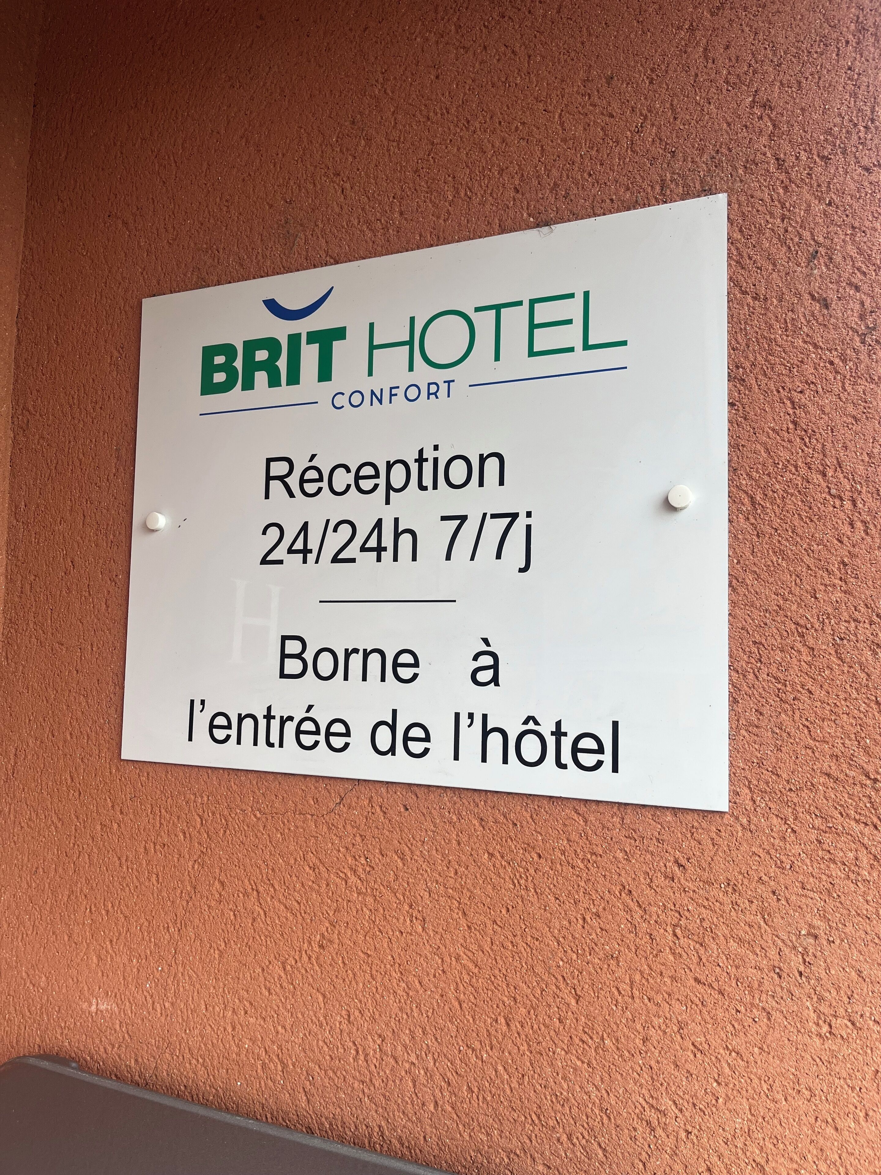 Señal del Brit Hotel Comfort que indica el horario de recepción: 24/24h, 7/7 días, y señala que está en la entrada del hotel.