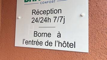 Señal del Brit Hotel Comfort que indica el horario de recepción: 24/24h, 7/7 días, y señala que está en la entrada del hotel.