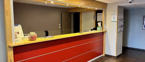 Una recepción con decoración en rojo y amarillo, un espejo encima y una cámara de seguridad en el techo.