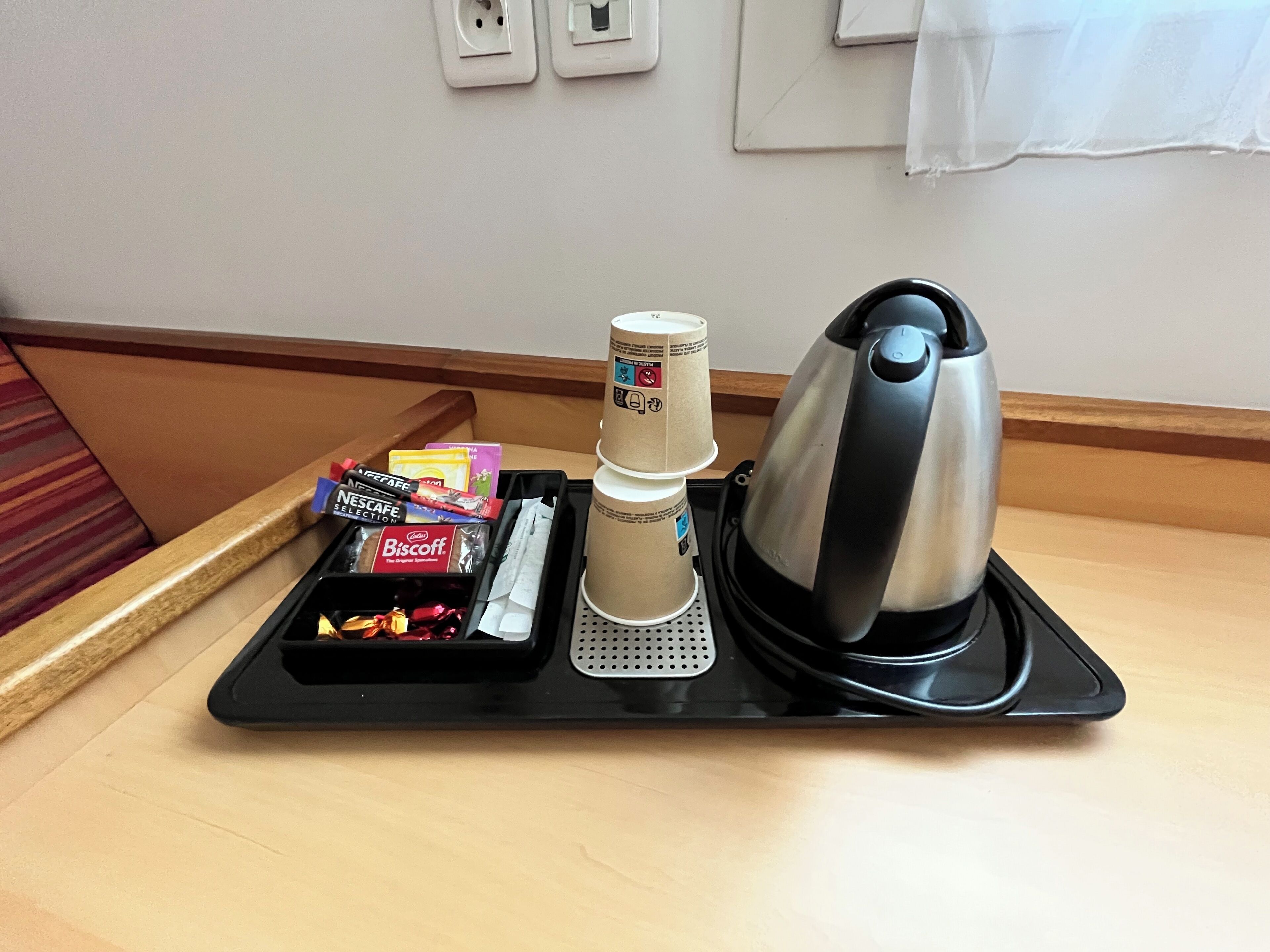 Un plateau avec une machine à café, des tasses empilées et quelques aliments, posé sur une table d’hôtel.