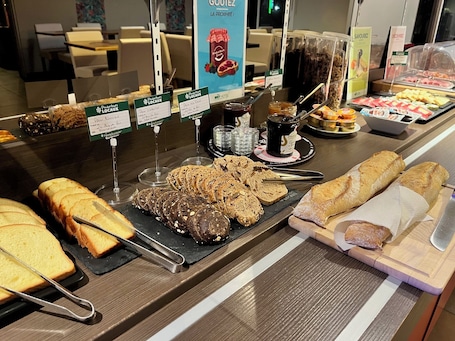 A breakfast buffet with various breads, pastries, and spreads.