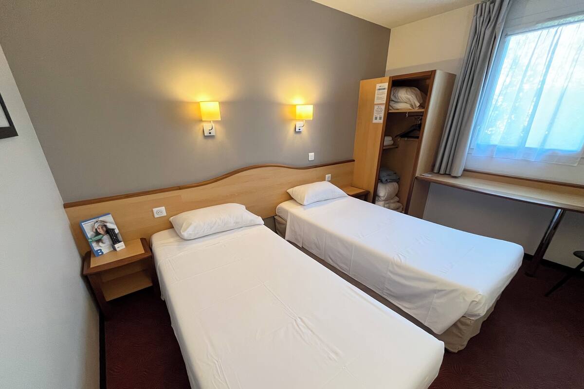 Een hotelkamer met twee enkele bedden, een houten hoofdbord, nachtlampjes, een bureau en een kledingkast.