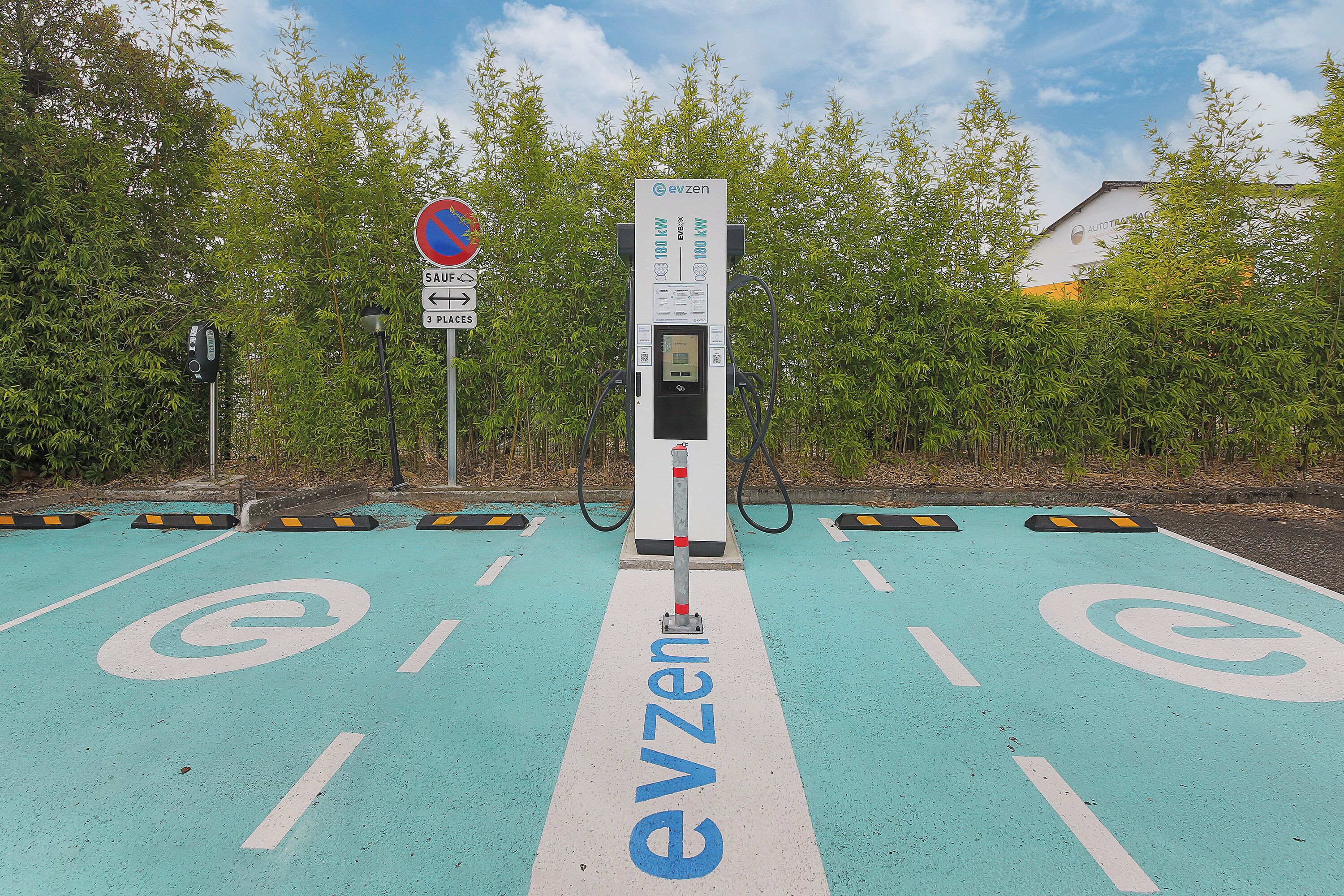 An EV Zen charging station with a clear path marked for electric vehicles, surrounded by greenery and a no parking sign.