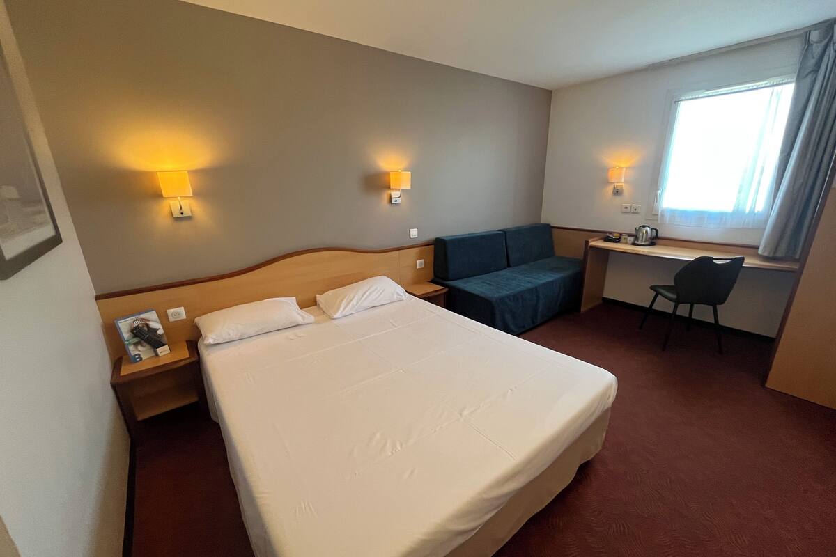 Een hotelkamer met een bed, een bureau, een stoel en twee wandlampen.