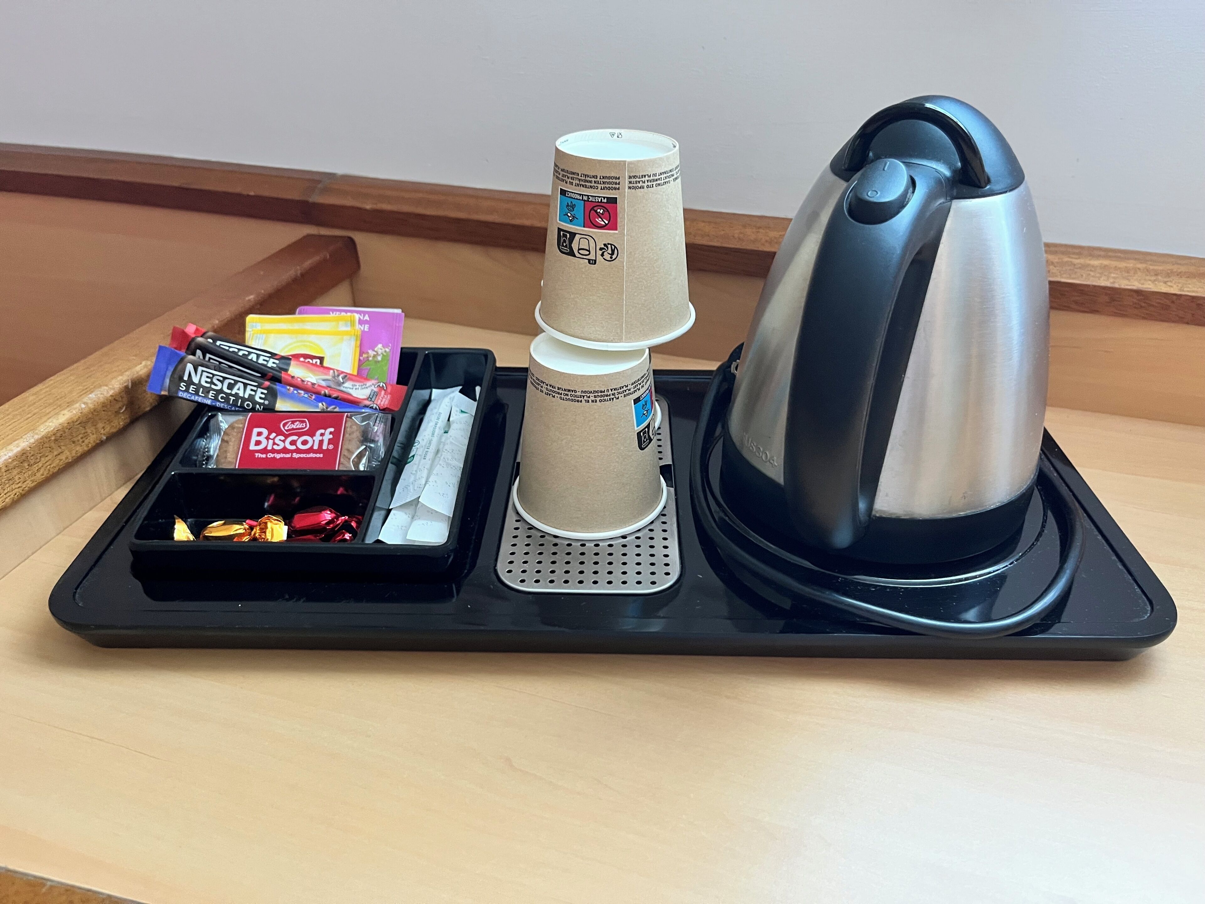 Ein Tablett mit einer Kaffeemaschine, gestapelten Papierbechern und verschiedenen Kaffeekapseln.