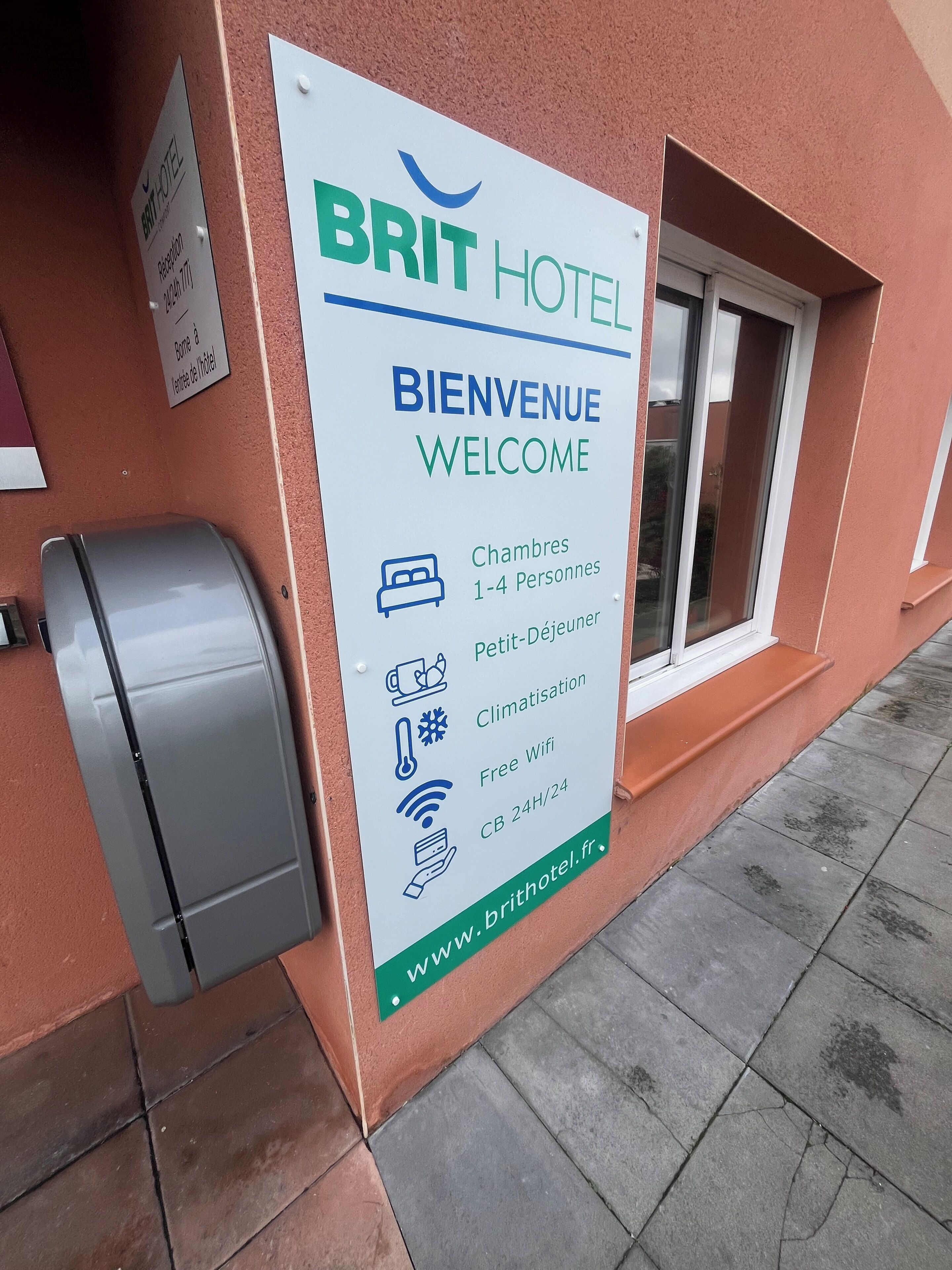 A sign for the Brit Hotel with amenities including rooms for 1-4 people, a small kitchenette, climate control, free WiFi, and 24-hour check-in/check-out.