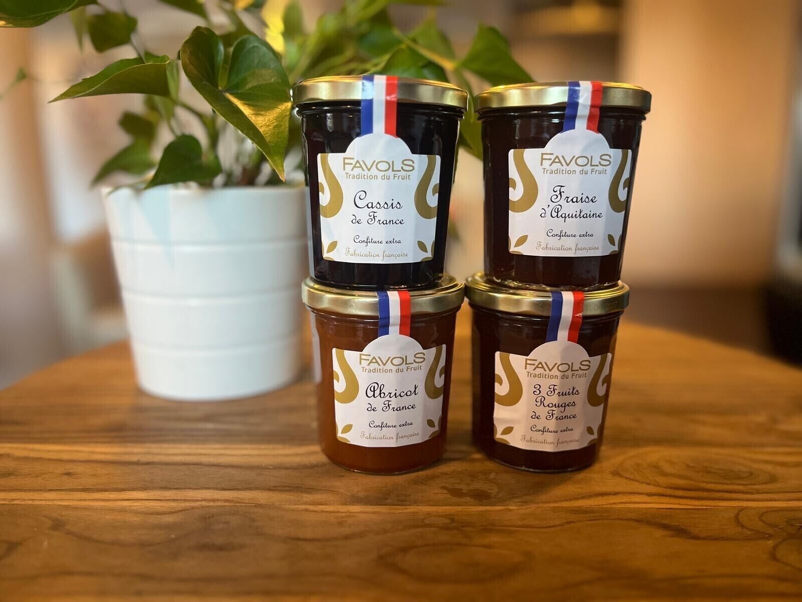 Trois pots de confiture Favols sont posés sur une table en bois, avec un pot blanc en arrière-plan.