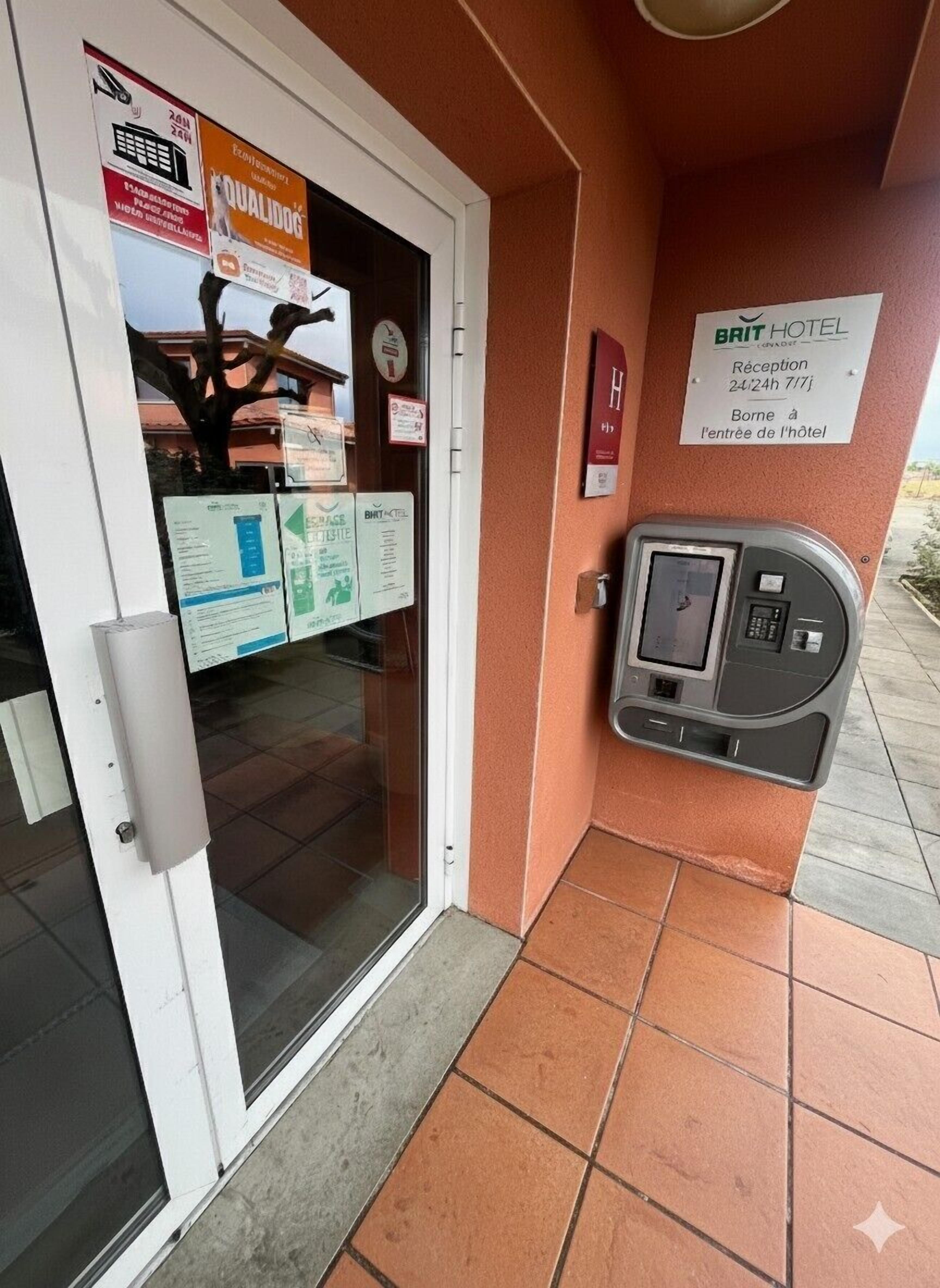 Un espace d’accueil d’hôtel comprenant un comptoir de réception, un lecteur de cartes-clés numériques et des affiches d’information sur le mur.