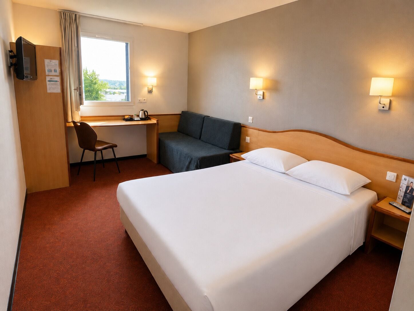 A hotel room with a bed, a desk, a chair, a sofa, and two wall-mounted lamps.