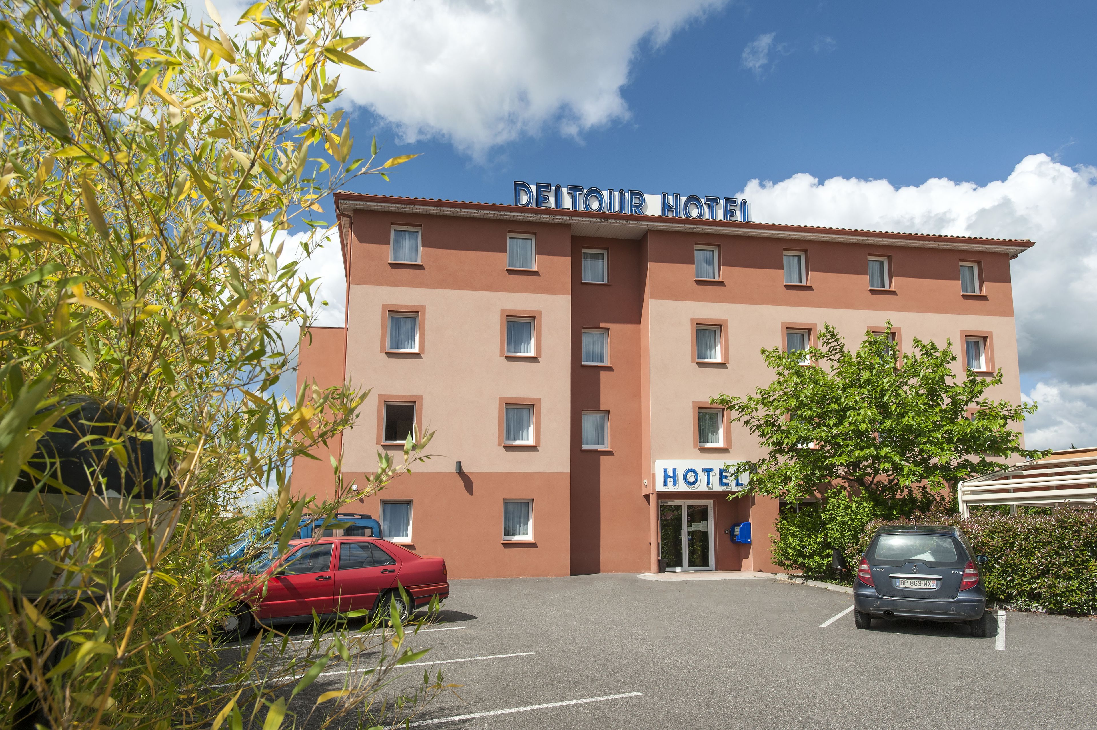 Un hotel con un cartel que dice "DELTOUR HOTEL" y un estacionamiento con coches.