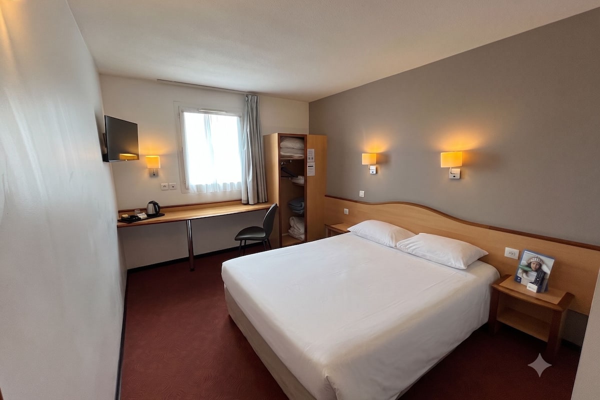 Een hotelkamer met een bed, bureau, stoel en twee nachtkastjes.