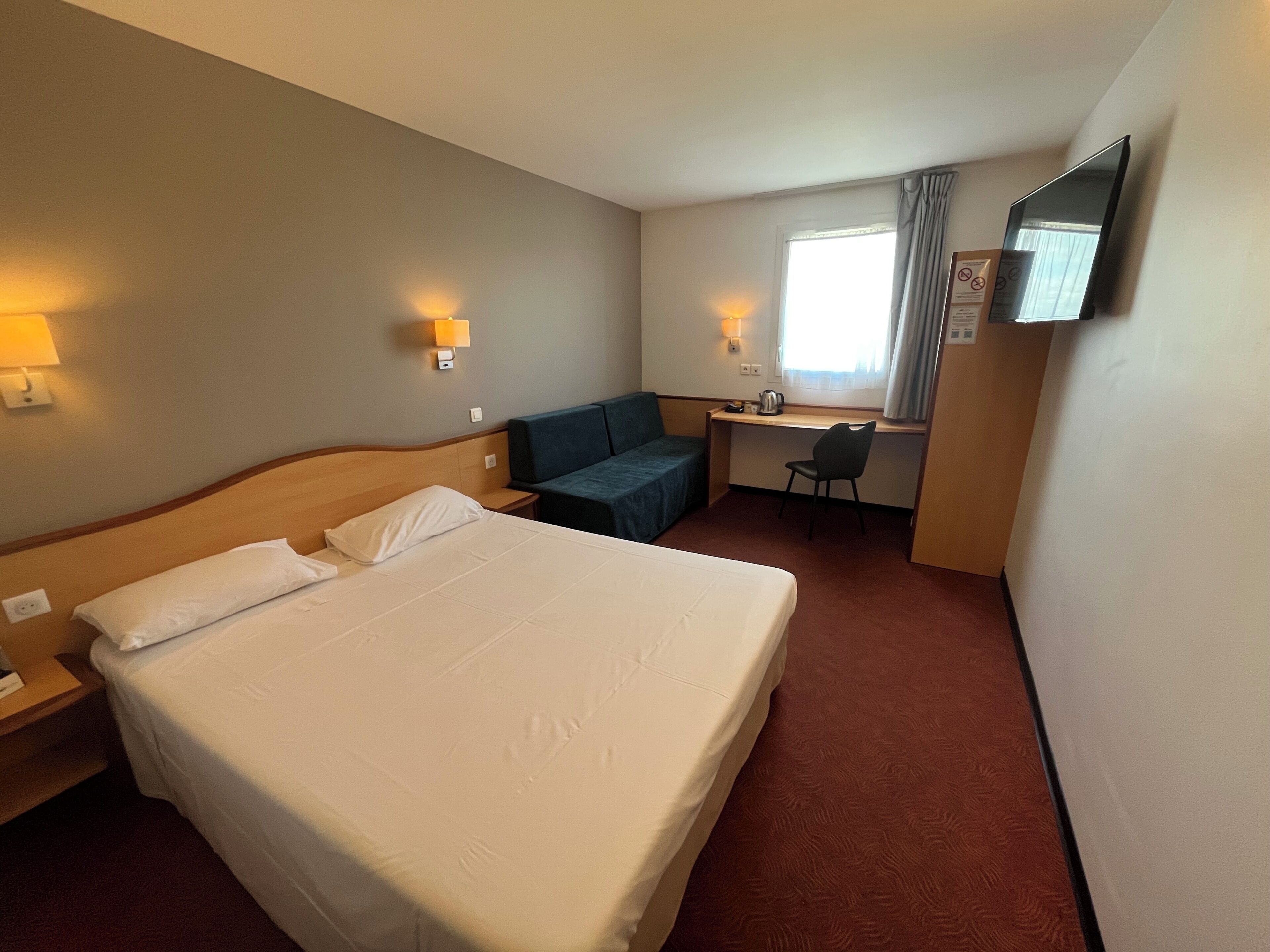 A hotel room with a large bed, a desk, a chair, and a television.