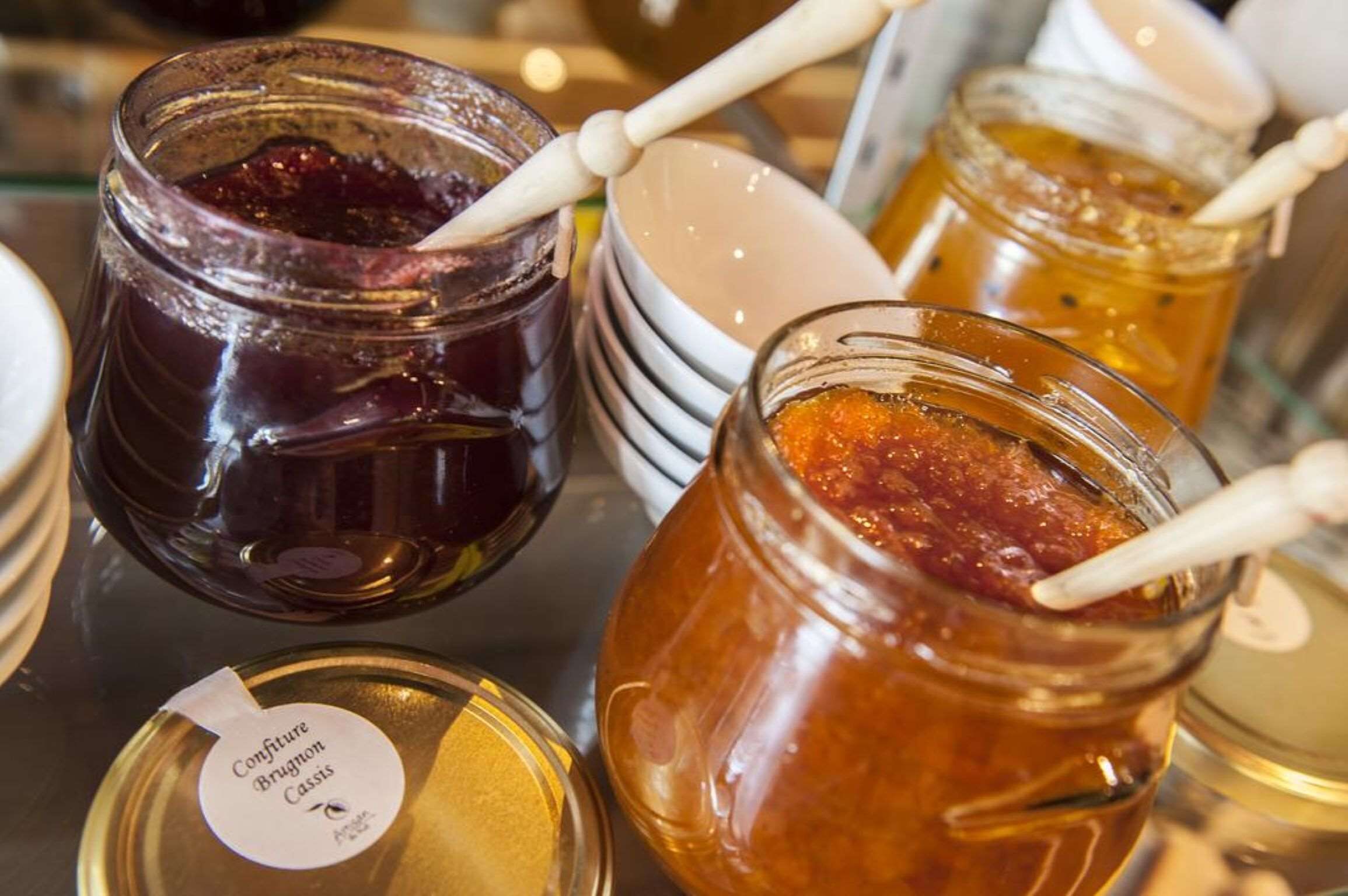 Jars of preserves on a table with a label reading "Confiture Brugnolon Cassis."