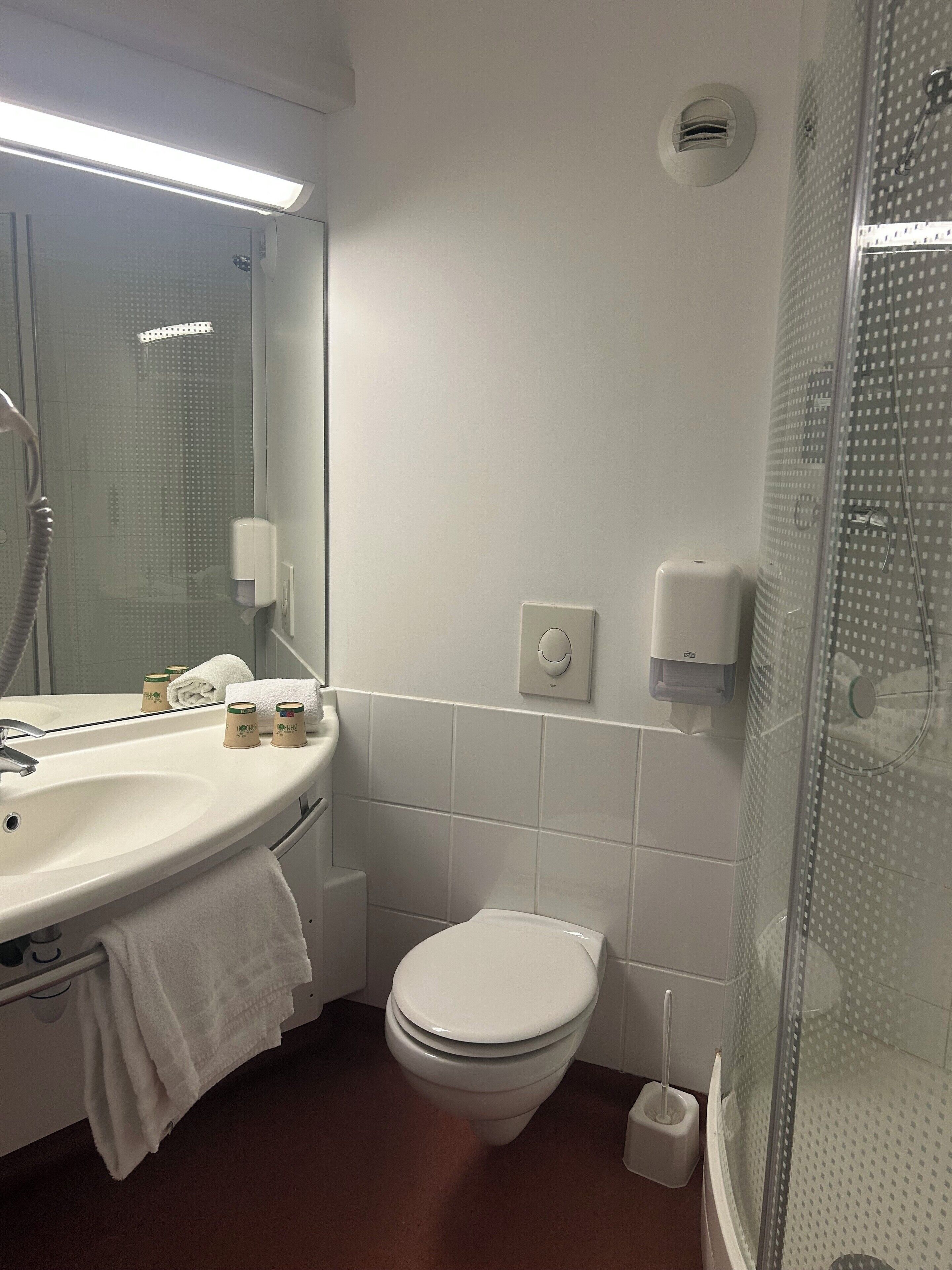 A modern bathroom with a white sink, mirror, and toilet. There is a glass shower enclosure and a hand dryer on the wall.