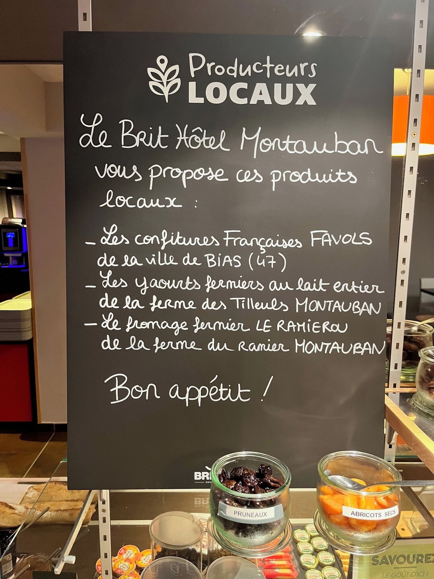 A signboard listing local products offered by Le Brit Hotel Montauban, including French cheeses, farm-fresh yogurt, and farm-fresh jams.