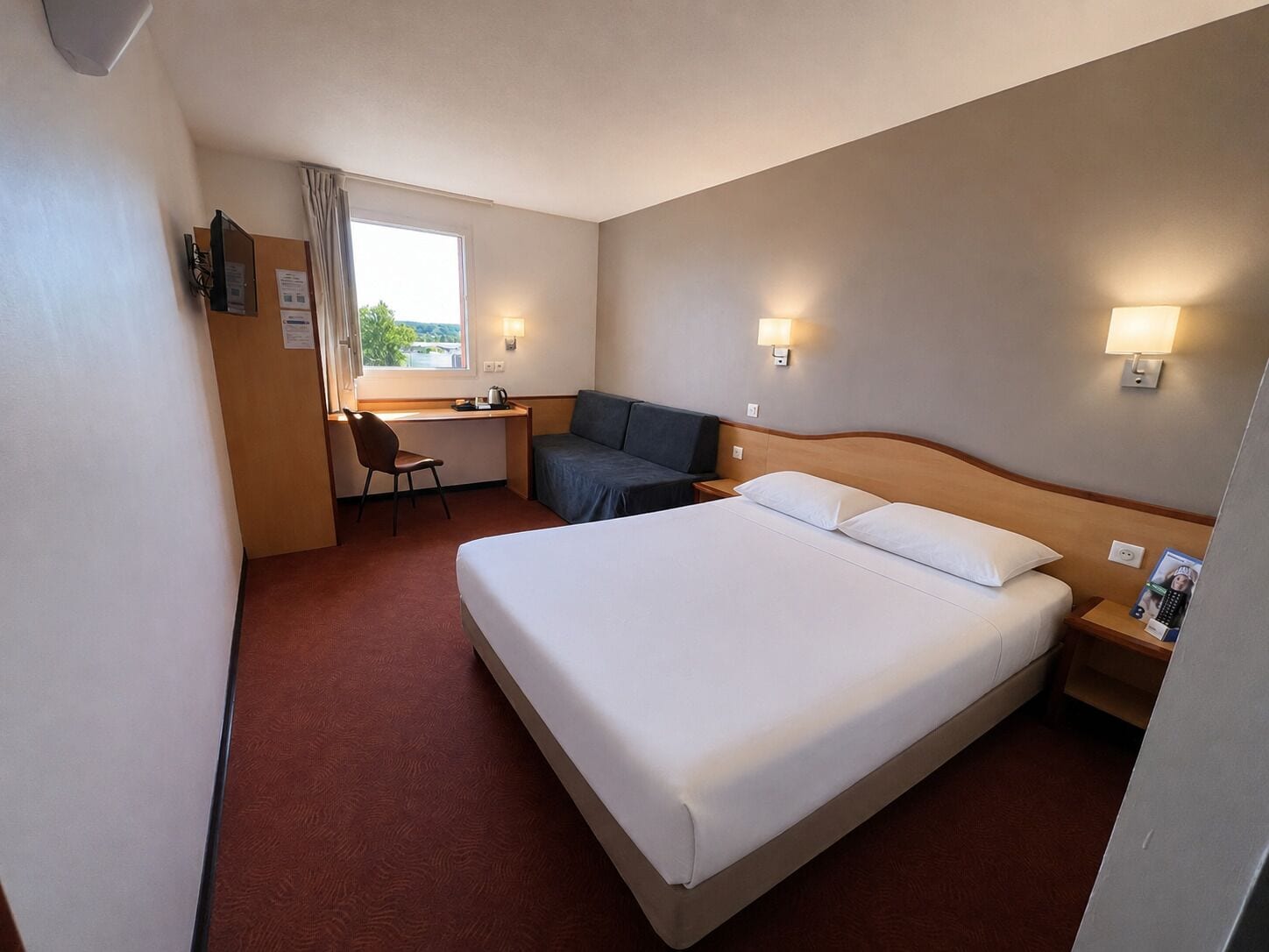 A hotel room with a bed, a desk, a chair, and a couch.