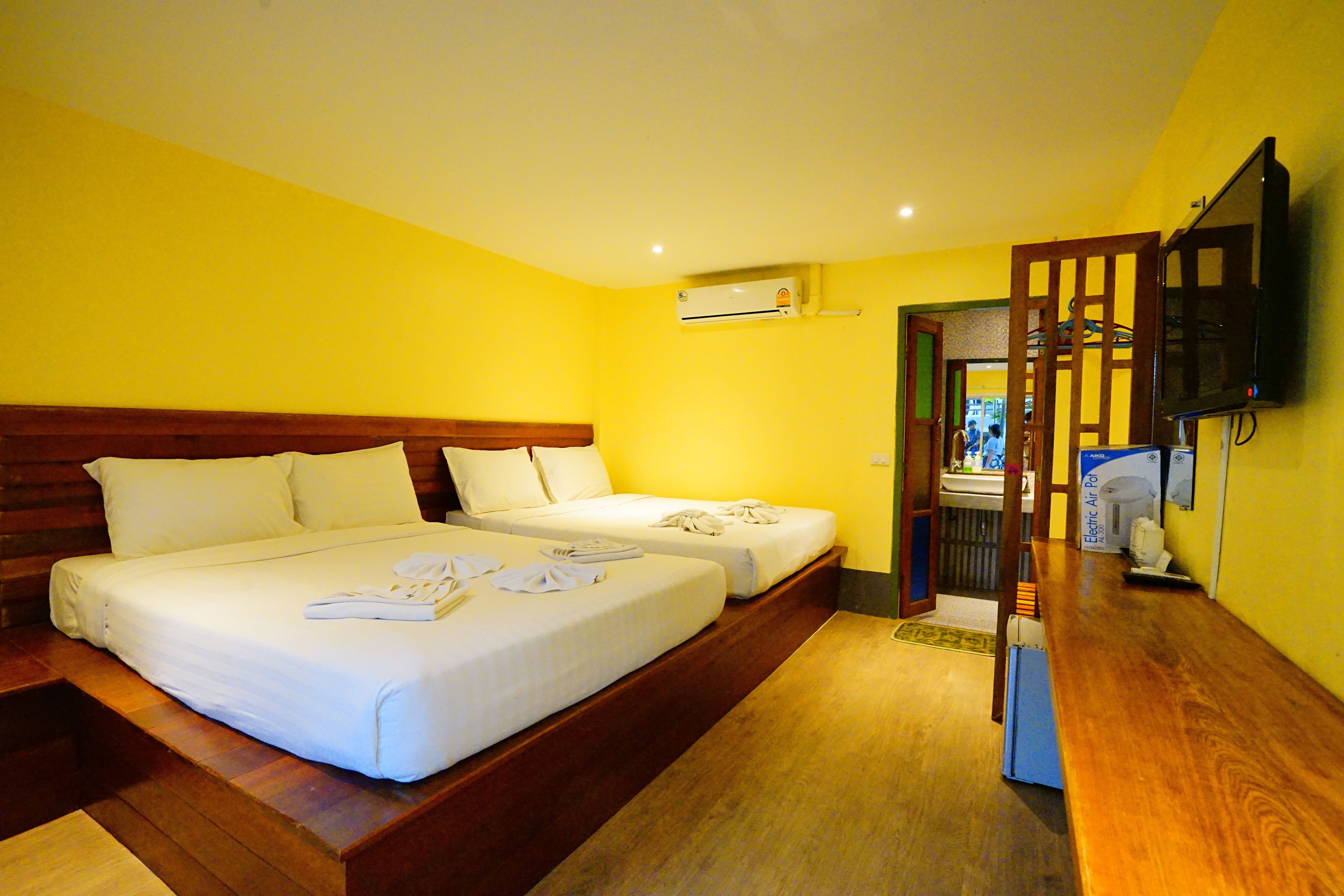 A hotel room with two beds, wooden headboards, a flat-screen TV, and an air conditioning unit.